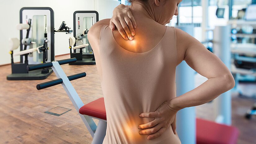 Eine Dame zeigt ihre Schmerzzonen am Rücken.