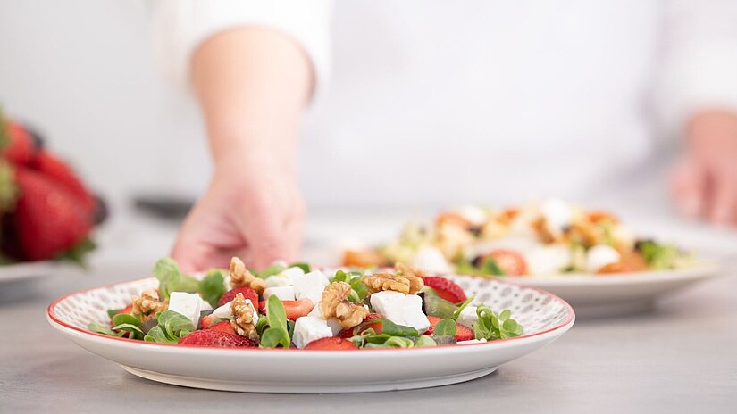 Ein angerichteter Salatteller wird von einem Koch gehalten.